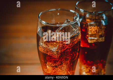 Belle cold fizzy soda cola avec glaçons ice dans les verres gobelet sur l'ancien fond de bois avec de l'espace libre. shallow dof. Banque D'Images