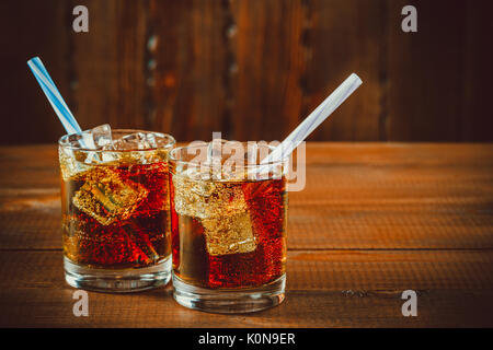 Beau verre de coca avec des glaçons avec une chaudière de pailles dans les verres sur fond de bois avec de l'espace libre. shallow dof. Banque D'Images