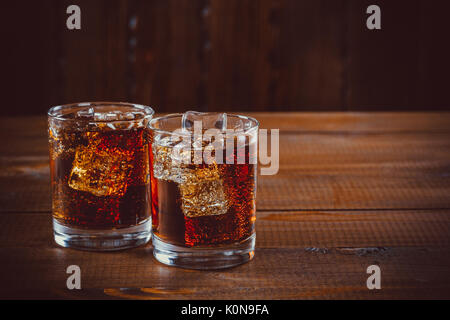 Belle cold fizzy soda cola avec glaçons ice dans les verres gobelet sur l'ancien fond de bois avec de l'espace libre. shallow dof. Banque D'Images