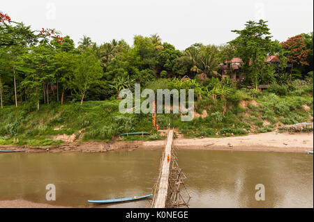 Un groupe de moines bouddhistes vêtus de safran traversent un pont de bambou sur la rivière Nam Khan, Louand Prabang, Laos. Banque D'Images