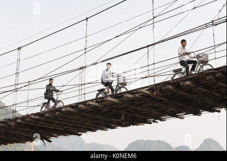 Shoolboys la bicyclette sur un pont à Vang Vieng, Laos. Banque D'Images