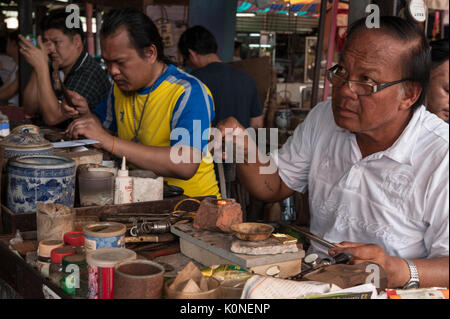Un brazes fabricant de bijoux une bague, l'un des nombreux services de réparation fourni par Goldsmiths au marché Talat Sao à Vientiane. Banque D'Images
