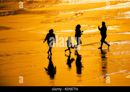 La silhouette d'une famille de vacanciers s'amuser sur la plage au coucher du soleil. Banque D'Images