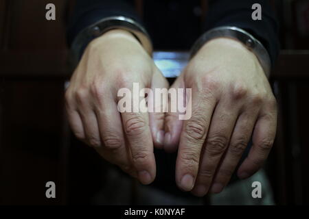 Abstract. Les mains du prisonnier sur un treillis en acier de près. L'homme en prison, menottes. Détail des mains avec de l'acier des menottes. Banque D'Images