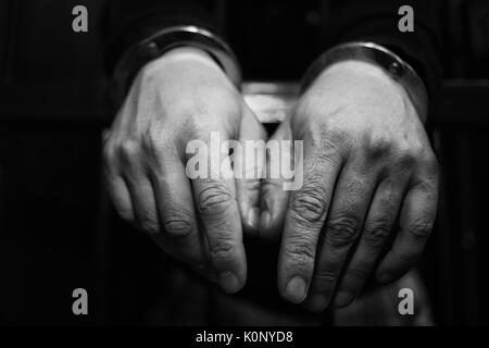 Abstract. Les mains du prisonnier sur un treillis en acier de près. L'homme en prison, menottes. Détail des mains avec de l'acier des menottes. Banque D'Images