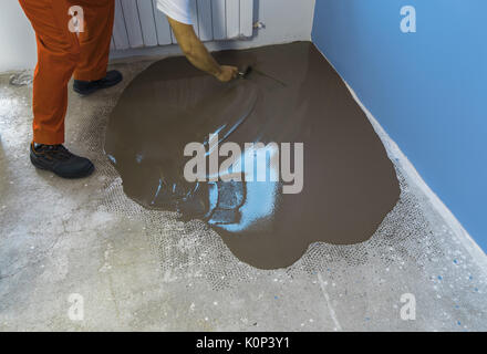 Vacances en construction. travailleur met une chape d'auto-nivellement sur plancher de béton Banque D'Images