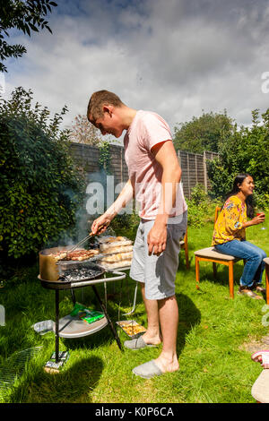 Un jeune homme à la cuisson des aliments sur un barbecue, Sussex, UK Banque D'Images