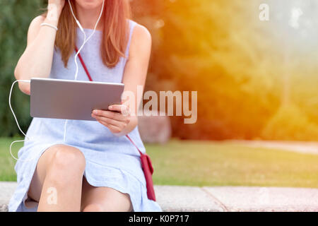 Voir de belles woman listening to music in headphones assis en plein air, dans le parc Banque D'Images