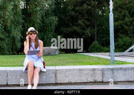 Voir de belles woman listening to music in headphones assis en plein air, dans le parc Banque D'Images