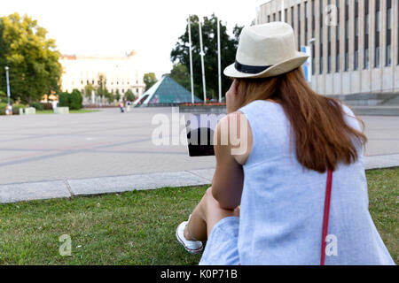 Voir de belle jeune femme de l'arrière à l'écoute de la musique dans les écouteurs assis en plein air, dans le parc Banque D'Images