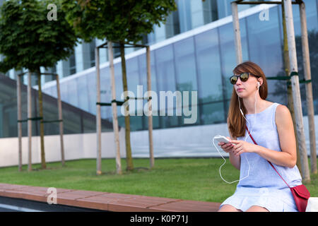 Voir de belles woman listening to music in headphones assis en plein air, dans le parc Banque D'Images