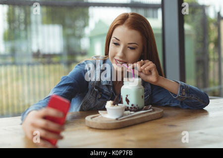 Femme de prendre un verre tout en ayant des selfies at table in cafe Banque D'Images