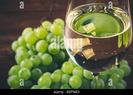 Plein de vin blanc dans des verres à vin avec un tas de raisins verts, sur un fond de bois Banque D'Images