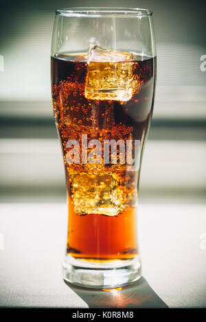 Beau verre de coca avec des glaçons dans un verre sur un arrière-plan de la fenêtre grise avec de l'espace libre Banque D'Images