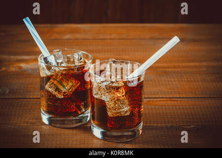 Beau verre de coca avec des glaçons avec une chaudière de pailles dans les verres sur fond de bois avec de l'espace libre Banque D'Images