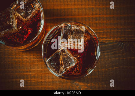 Belle cold fizzy soda cola avec glaçons ice dans les verres gobelet sur l'ancien fond de bois avec de l'espace libre Banque D'Images