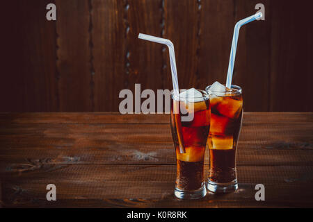 Beau verre de coca avec des glaçons avec une chaudière de pailles dans les verres sur fond de bois avec de l'espace libre Banque D'Images