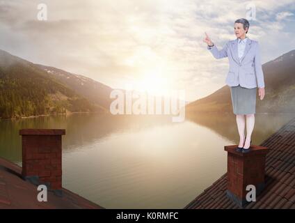 Digital composite of Businesswoman standing sur toits avec cheminée et le paysage de montagne lac Banque D'Images