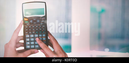 Les mains coupées de businesswoman using calculator contre close-up de la fenêtre Banque D'Images