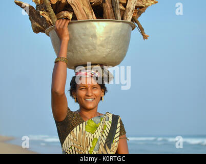 La jeune femme indienne d'Orissan de la communauté de pêcheurs locale de Puri porte une lourde charge de bois de chauffage sur sa tête. Banque D'Images