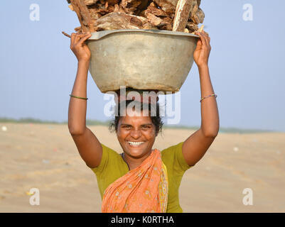 Une femme indienne d'Orissan de la communauté de pêcheurs locale de Puri porte une lourde charge de bois de chauffage sur sa tête et sourit pour l'appareil photo. Banque D'Images