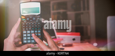 Les mains coupées de businesswoman using calculator contre image flou artistique de tablette numérique et fichiers par lamp Banque D'Images