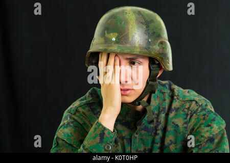 Beau triste jeune soldat en uniforme qui souffrent de stress avec sa main sur son visage, dans un fond noir Banque D'Images