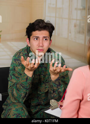 Malheureux beau jeune soldat en uniforme, souffrant de stress post-traumatique après la guerre, parlant à la thérapeute dans un centre de santé médical, dans un contexte avec des copeaux Banque D'Images