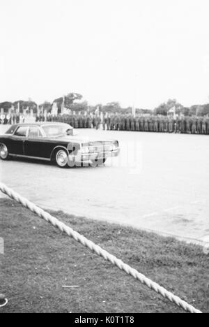 Voiture noire, avec drapeau, conduire sur une route au-delà d'un grand groupe de soldats à l'attention, photo provenant du côté de la route, derrière la zone délimitée, Vietnam, 1969. Banque D'Images