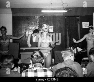 Montrer l'USO, les soldats américains vu de derrière, regarder trois femme en révélant bikinis dance séductrice lors d'un spectacle au Vietnam pendant la guerre du Vietnam, un homme jouant un clavier sur scène derrière les femmes, 1965. Banque D'Images