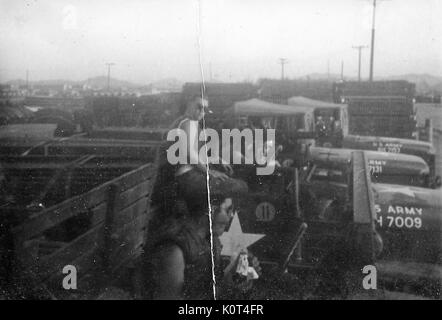 Une photo de deux soldats de l'armée des États-Unis assis dans le lit d'un camion militaire M35, d'autres camions, les matériaux de construction, et la base de l'Armée ils sont situés sur sont vus dans l'arrière-plan, Vietnam, 1967. Banque D'Images