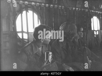 Une rangée de trois soldats de l'armée des États-Unis dans l'intérieur de l'aéronef, un soldat tient une caméra personnelle tandis qu'un autre tient son fusil de combat, Vietnam, 1967. Banque D'Images