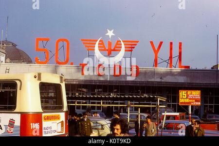 En dehors de la scène de la gare, du terminal de Sirkeci à Istanbul, Turquie, novembre 1973. Un grand panneau au-dessus de l'entrée indique '50 yil tcdd", célébrant le 50e anniversaire à venir de l'État turc de fer. les véhicules, des civils, et les hommes en uniforme attendre en face de la gare. un bus à l'avant-plan dispose de la publicité pour les radios et télévisions Grundig. Banque D'Images