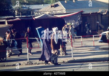 Scène de rue avec de nombreuses personnes à Kaboul, Afghanistan, novembre 1975. un homme et une femme voilée d'une burka afghane traditionnelle marcher ensemble au centre du châssis. Banque D'Images