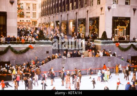 Vue sur la patinoire du Rockefeller Center, rempli de patinage de visiteurs pendant la saison de Noël, au Rockefeller Plaza, Manhattan, New York, décembre 1969. Des foules de gens line l'escalier et la promenade menant à la 5e Avenue. Banque D'Images