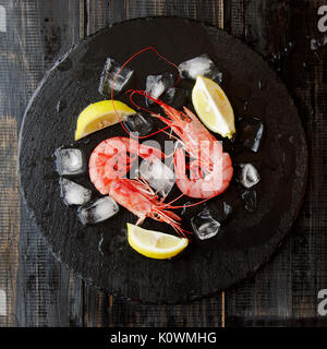 Deux crevettes crus avec du citron et des cubes de glace sur un tableau noir, selective focus Banque D'Images