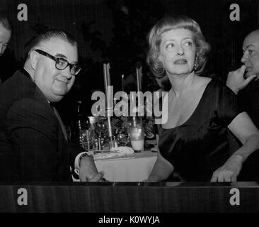 Bette Davis, assis à une table de banquet avec un homme non identifié, tournant autour de son président et à la recherche de son droit, dans une pièce sombre au cours d'un dîner, Hollywood, Californie, Hollywood, Californie, 1950. Crédit photo Smith Collection/Gado/Getty Images. Banque D'Images