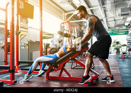 Fille sportive faisant des exercices de poids corporel avec l'aide de son entraîneur personnel à la salle de sport. Banque D'Images