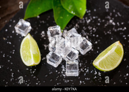 Ice Cube avec des tranches de citron vert et le sel sur la table sombre contexte Banque D'Images