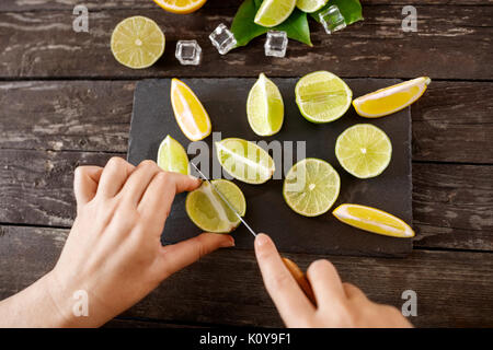 Des aliments sains et de manger. femme coupant les citrons sur une planche à découper noire Banque D'Images