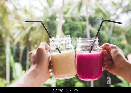 Deux fruits colorés dans les mains. L'été et l'ambiance tropicale. Mélangé à froid, des boissons et de bananes smoothie aux fruits du dragon. Cliquez lunettes par deux mains Banque D'Images