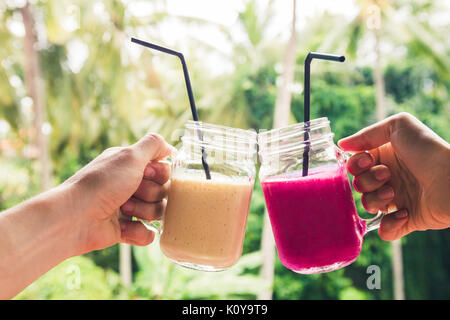 Deux fruits colorés dans les mains. L'été et l'ambiance tropicale. Mélangé à froid, des boissons et de bananes smoothie aux fruits du dragon. Cliquez lunettes par deux mains Banque D'Images