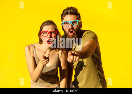 Hey you ! Homme barbu, des jeunes adultes et cute brunette pointer du doigt et à la recherche à l'appareil photo. Sur fond jaune. Piscine, studio shot Banque D'Images