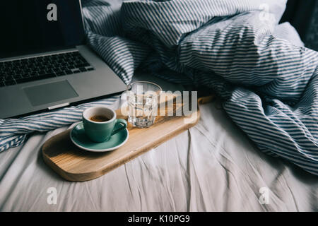 Belle matinée à travailler au lit essentials : ordinateur portable et un nouveau café le matin avec de belles d'épaisseur sur un en bois crème fait-main rustique le bac Banque D'Images