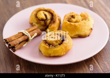 Trois petits pains à la cannelle servi et prêt à manger sur la plaque rose Banque D'Images