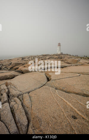 Peggy's Point Lighthouse au cours d'un jour brumeux, venteux avec touristes marcher sur les rochers. Banque D'Images