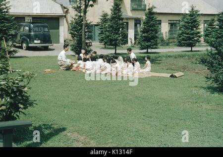 L'école du dimanche, deux japonais l'homme avec un grand groupe d'enfants sur un matelas de paille, sur un champ dans la mission méthodiste wesleyenne, Japon, 1952. Banque D'Images