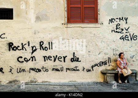 TROPEA, Calabre, Italie, avril 2014 : des graffitis dans une ancienne ville italienne de Calabre. Vieille Femme assise à côté d'un mur avec les mots "Rock'n roll peut nev Banque D'Images