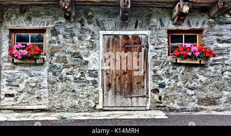 Vieille maison de ferme en pierres de champ avec porte en bois, deux fenêtres et des fleurs rouge vif Banque D'Images