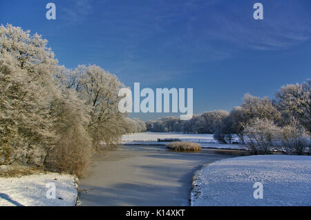 Rivière gelée dans un parc avec des champs couverts de neige et d'arbres Banque D'Images